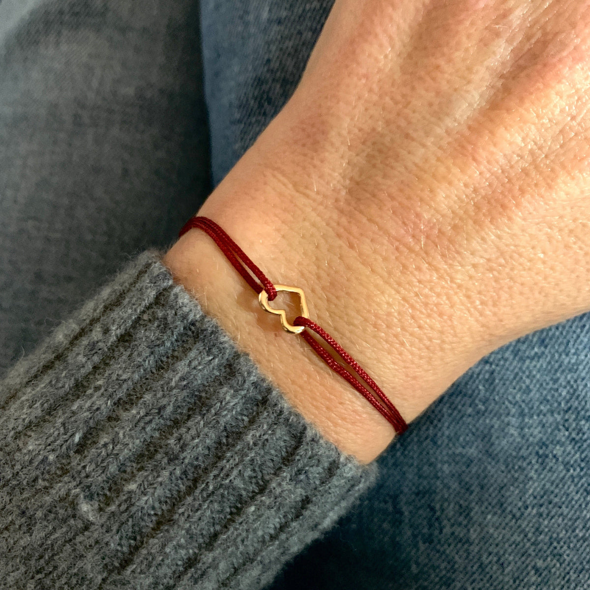 ANNA VON BERGMANN Armband GIDDY aus goldplattiertem Messing mit Herz an dunkelroter Kordel, getragen am Handgelenk