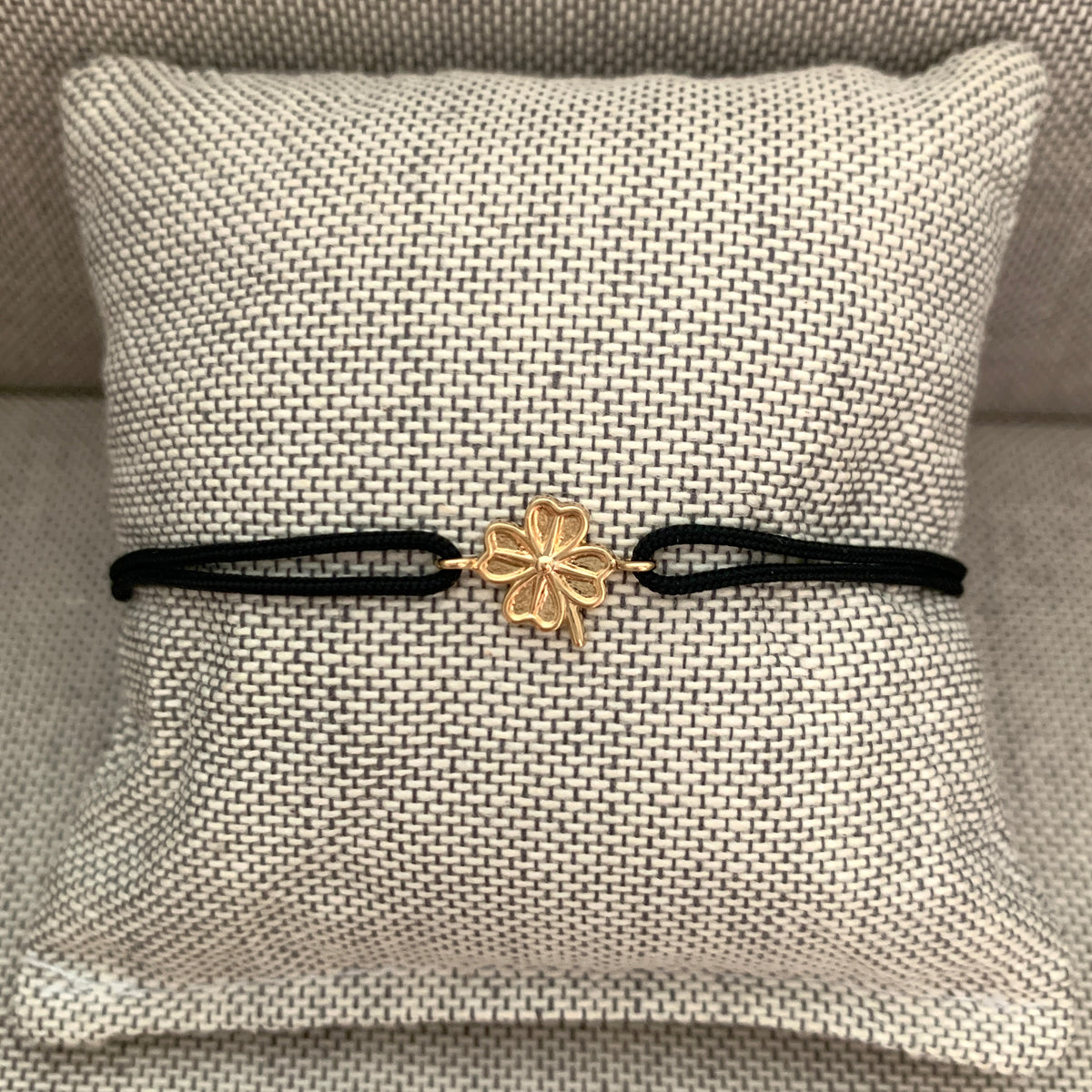 ANNA VON BERGMANN Armband GIDDY aus goldplattiertem Messing mit Kleeblatt an schwarzer Kordel auf Schmuckkissen