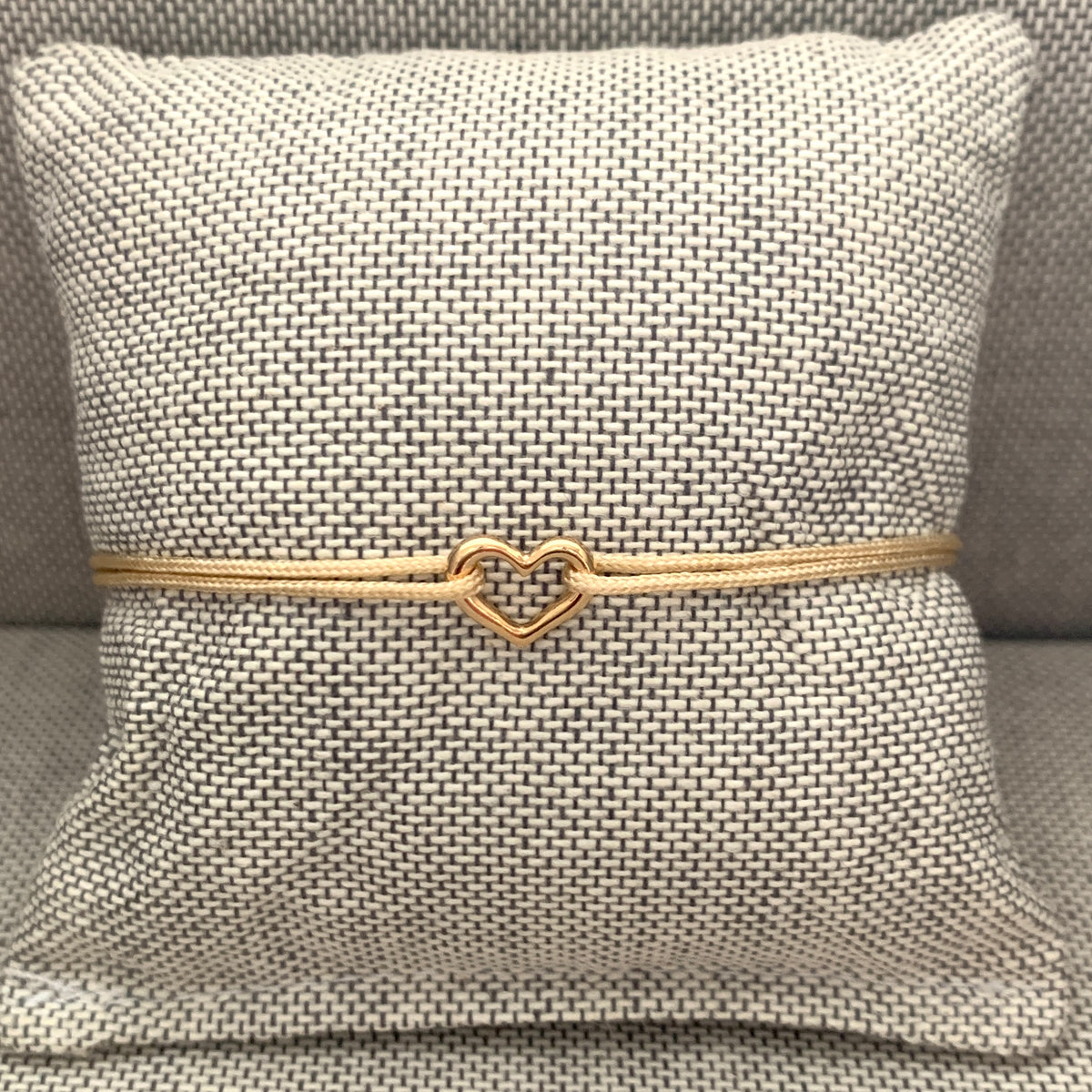 ANNA VON BERGMANN Kordelarmband GIDDY aus goldplattiertem Messing mit Herz, beige Kordel auf Schmuckkissen