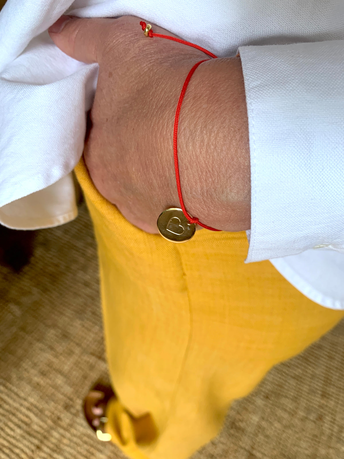 ANNA VON BERGMANN ARMBAND SMARTY BIG aus 18 kt goldplattiertem Messing, rote Kordel mit Herzplakette am Handgelenk getragen