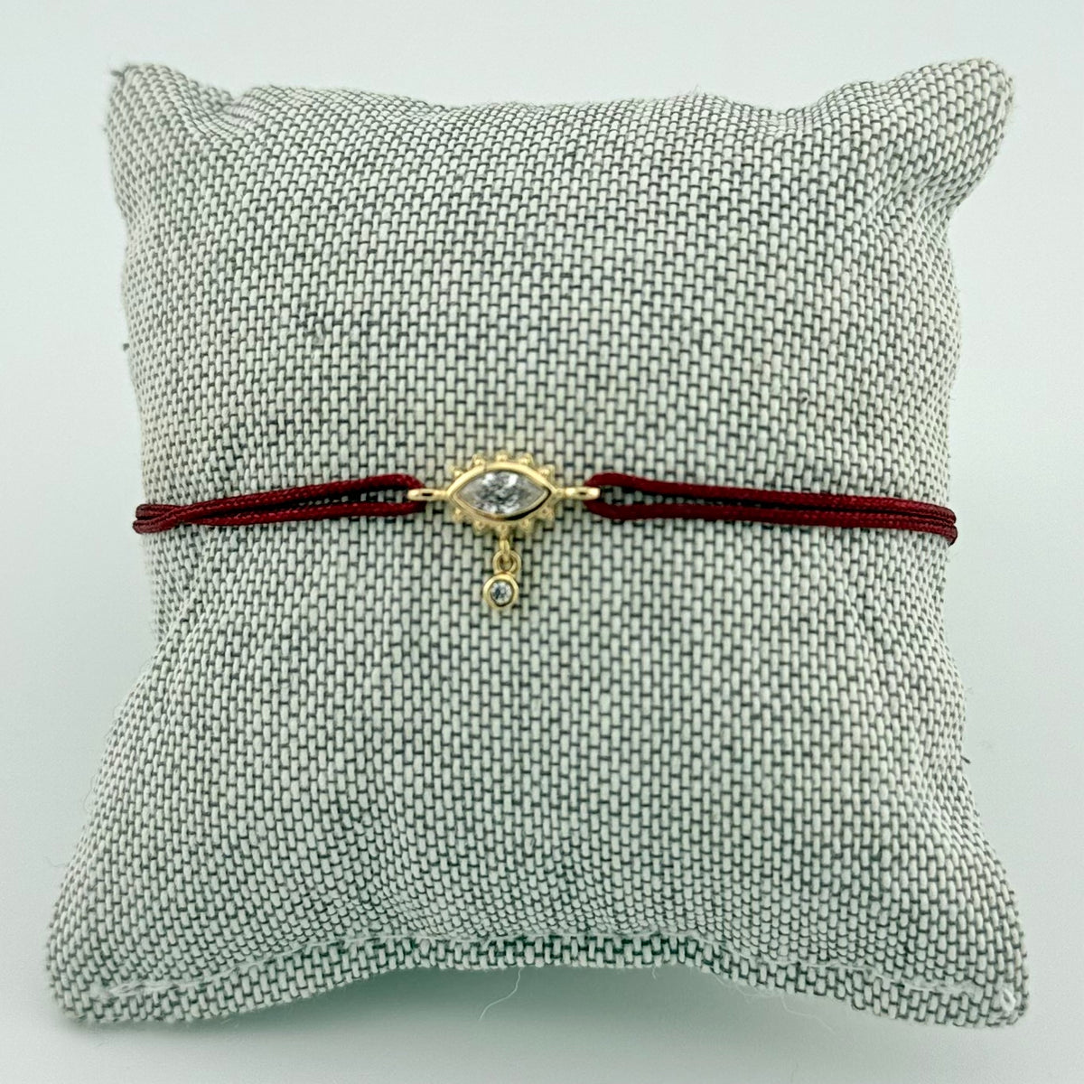 ANNA VON BERGMANN Armband GIDDY aus goldplattiertem Messing, Auge mit Zirkonia an dunkelroter Kordel auf Schmuckkissen