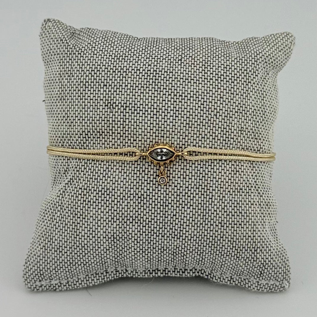 ANNA VON BERGMANN Kordelarmband GIDDY aus goldplattiertem Messing, Augenmotiv mit Zirkonia an beiger Kordel auf Kissen