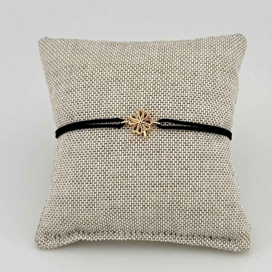 ANNA VON BERGMANN Kordelarmband GIDDY aus goldplattiertem Messing mit Kleeblatt, schwarze Kordel auf Kissen