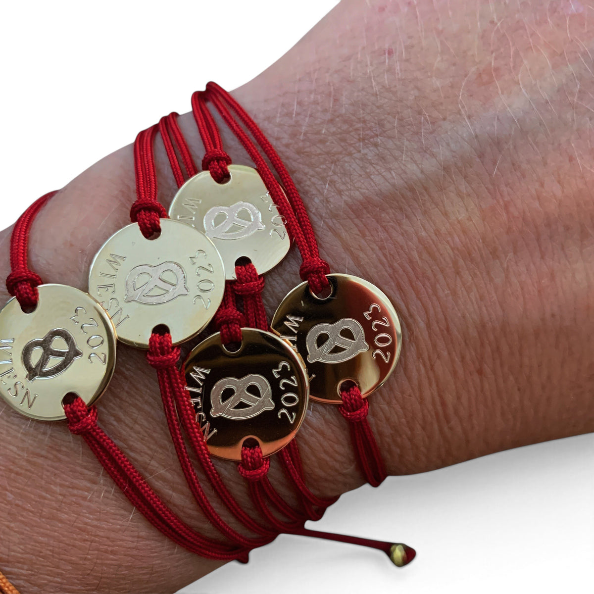 ANNA VON BERGMANN Armband mit roter Nylonkordel und goldplattierter runder Plakette mit Brezel-Gravur am Handgelenk