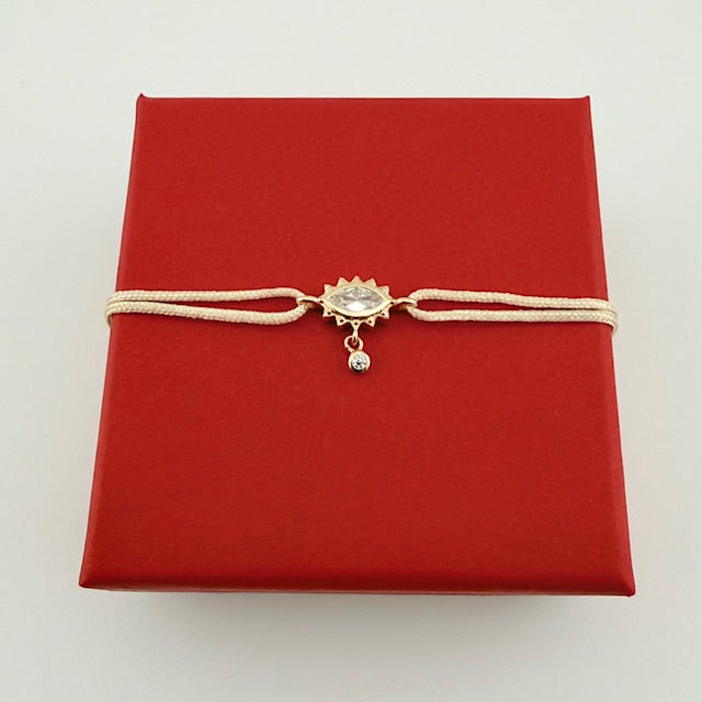 ANNA VON BERGMANN Kordelarmband GIDDY aus goldplattiertem Messing, Augenmotiv an heller Kordel auf roter Geschenkbox