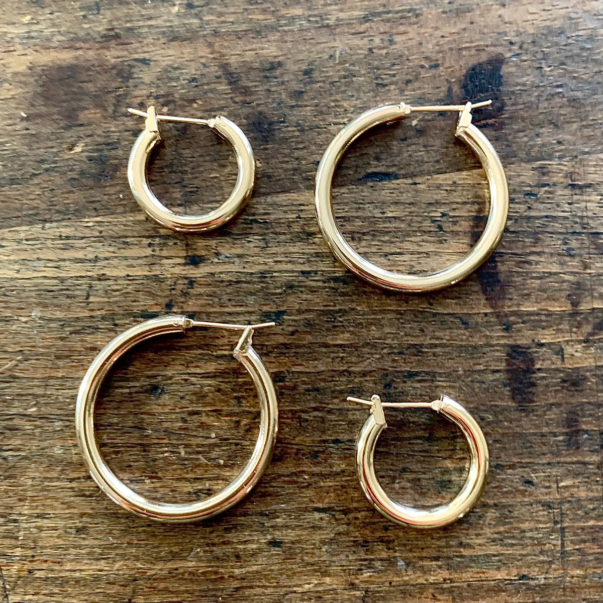 ANNA VON BERGMANN OHRCREOLEN TUBE aus 18 kt goldplattiertem Messing, zwei Größen nebeneinander auf Holz