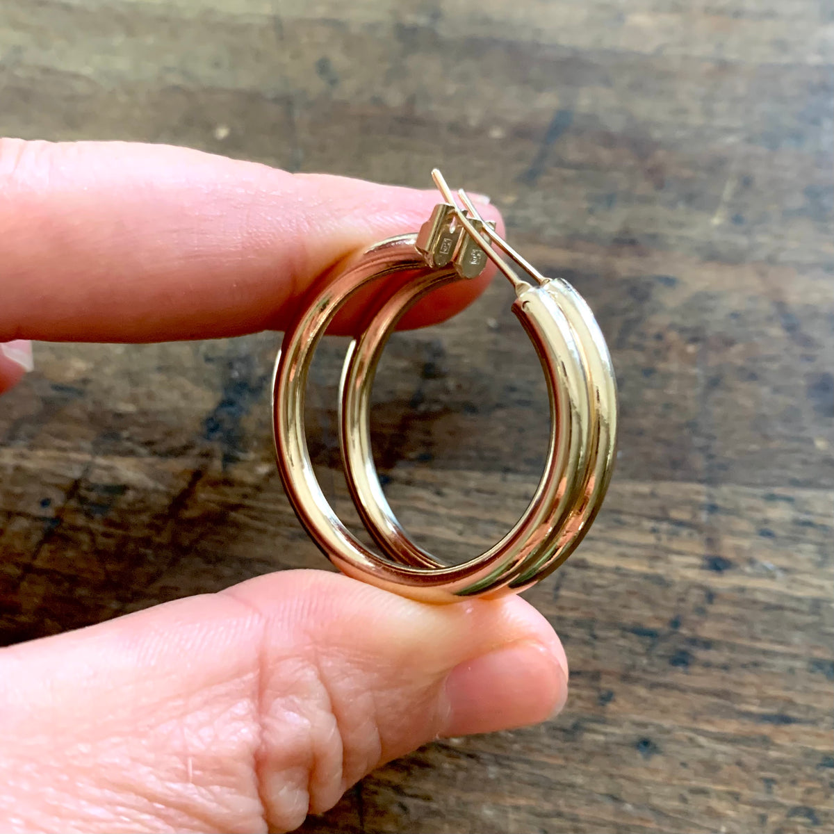 ANNA VON BERGMANN OHRCREOLEN TUBE aus 18 kt goldplattiertem Messing, zwei Creolen zwischen den Fingern gehalten