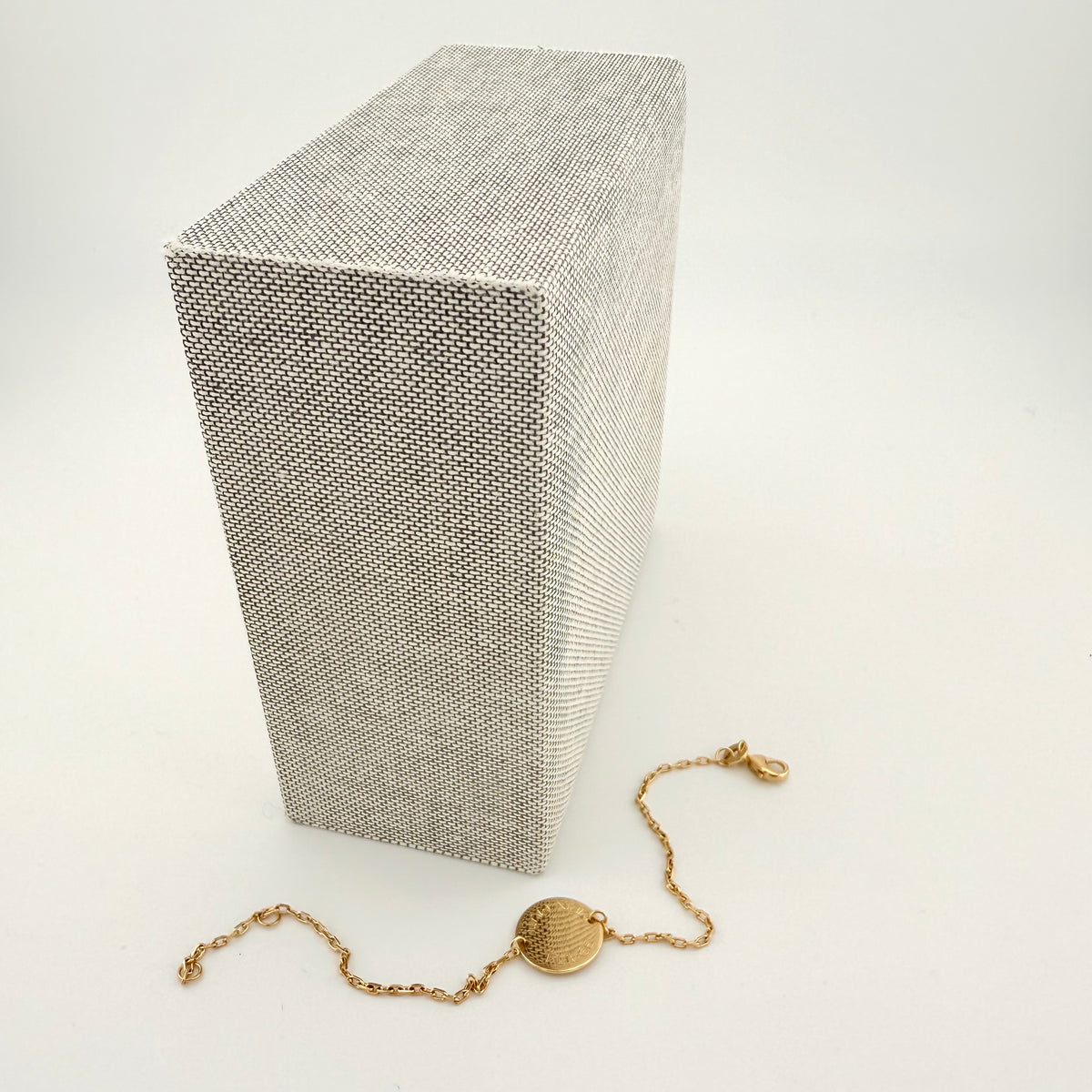 ANNA VON BERGMANN Armband DAISY mit Gravur aus 18 kt goldplattiertem Messing, liegend vor grauer Schmuckbox
