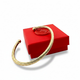 ANNA VON BERGMANN Armreif TWIST in goldplattiertem Messing mit Kordeloptik vor einer roten Geschenkbox