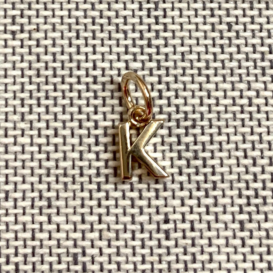 ANNA VON BERGMANN Buchstabenanhänger PETITE LETTRE aus 18 kt goldplattiertem Messing, Buchstabe K auf grauem Stoff