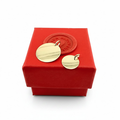 Zwei runde ANNA VON BERGMANN Anhänger aus 375er Echtgold zur individuellen Gravur auf einer roten Geschenkbox