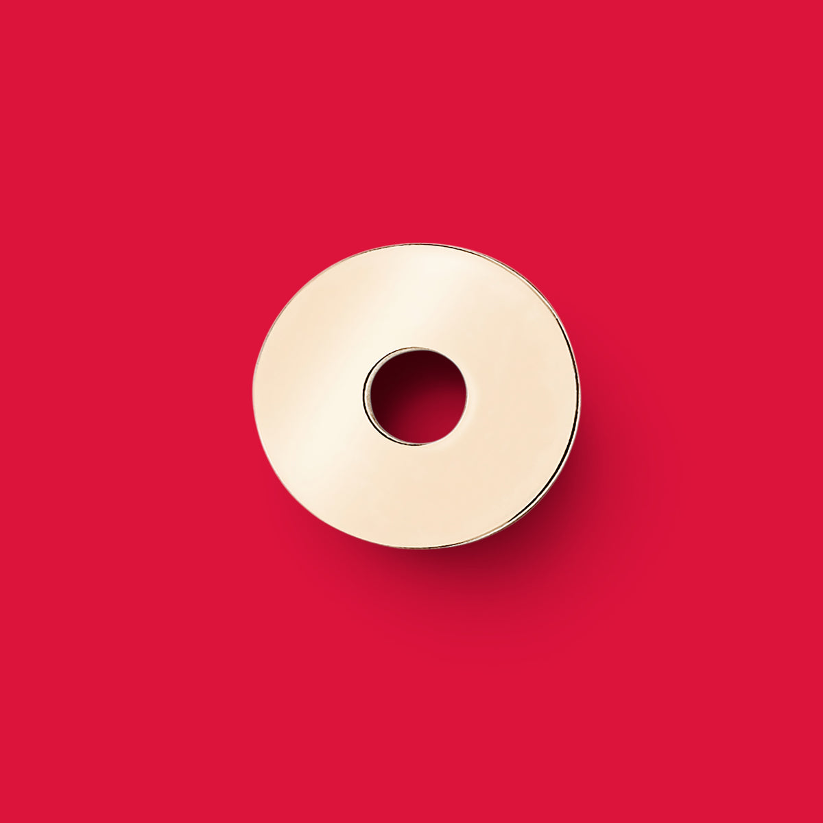 ANNA VON BERGMANN Donut Anhänger aus goldplattiertem Messing in runder Plakettenform vor rotem Hintergrund