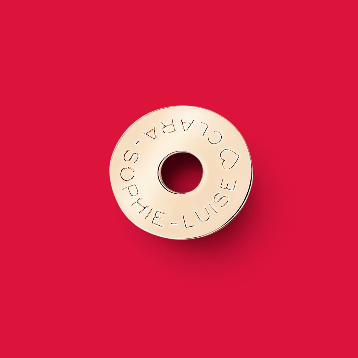 ANNA VON BERGMANN Donut Anhänger aus goldplattiertem Messing mit individueller Gravur auf rotem Hintergrund