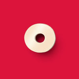 ANNA VON BERGMANN Donut Anhänger aus goldplattiertem Messing in runder Plakettenform vor rotem Hintergrund