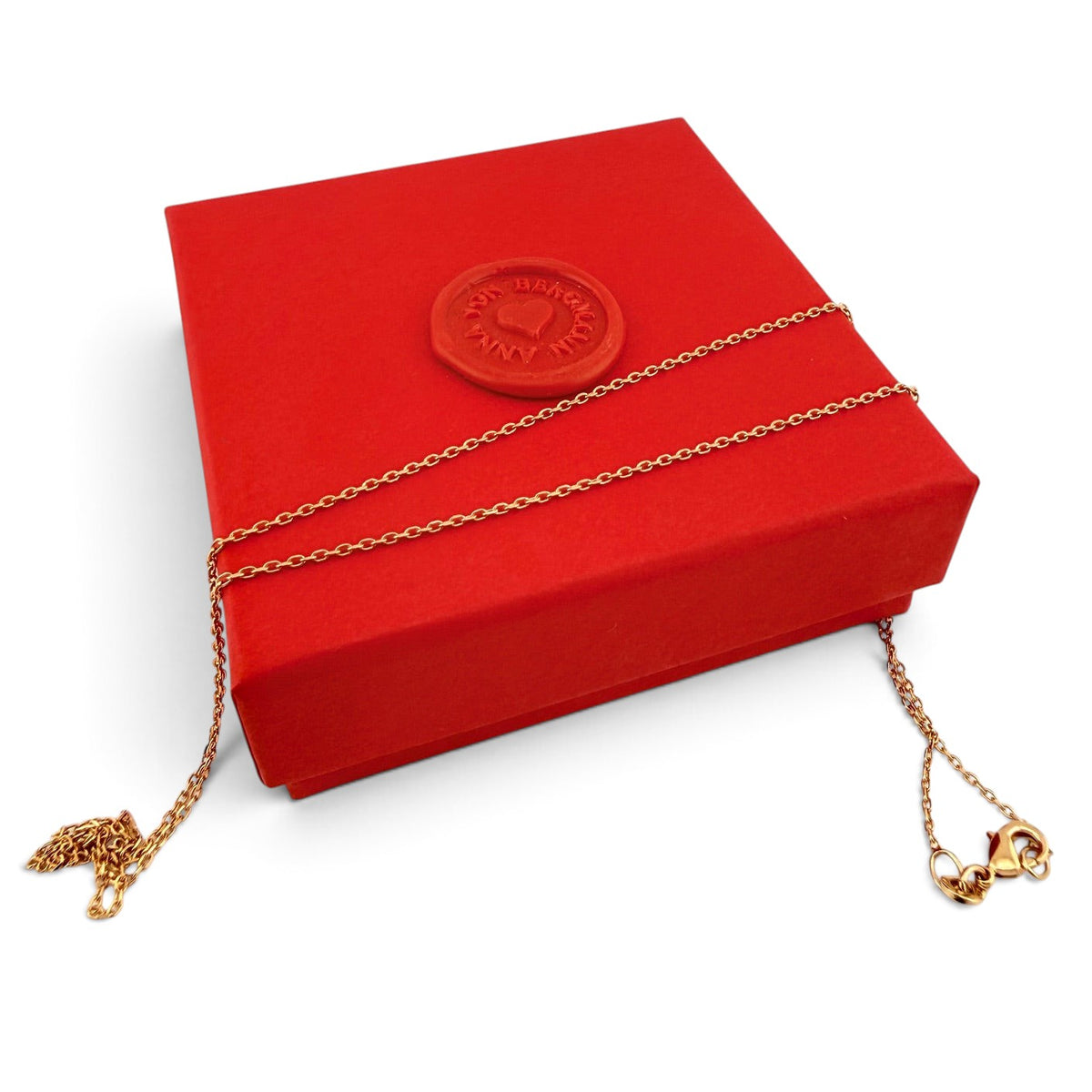 ANNA VON BERGMANN feine goldplattierte Ankerkette auf einer roten Geschenkbox mit Wachssiegel