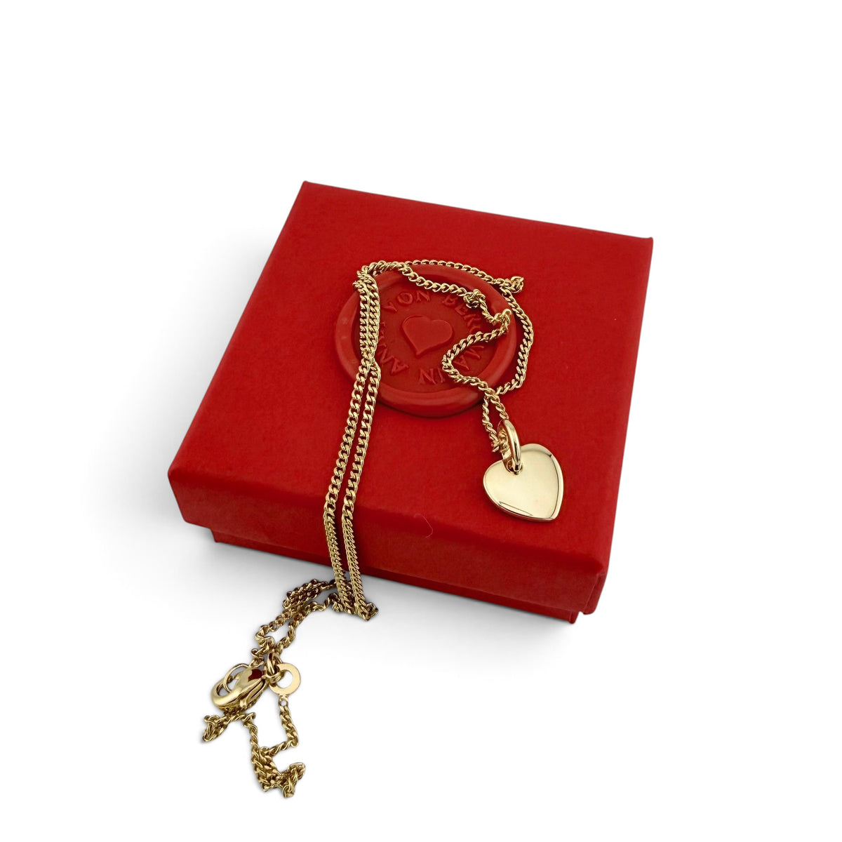 ANNA VON BERGMANN Kette mit herzförmigem Anhänger aus goldplattiertem Messing auf einer roten Geschenkbox