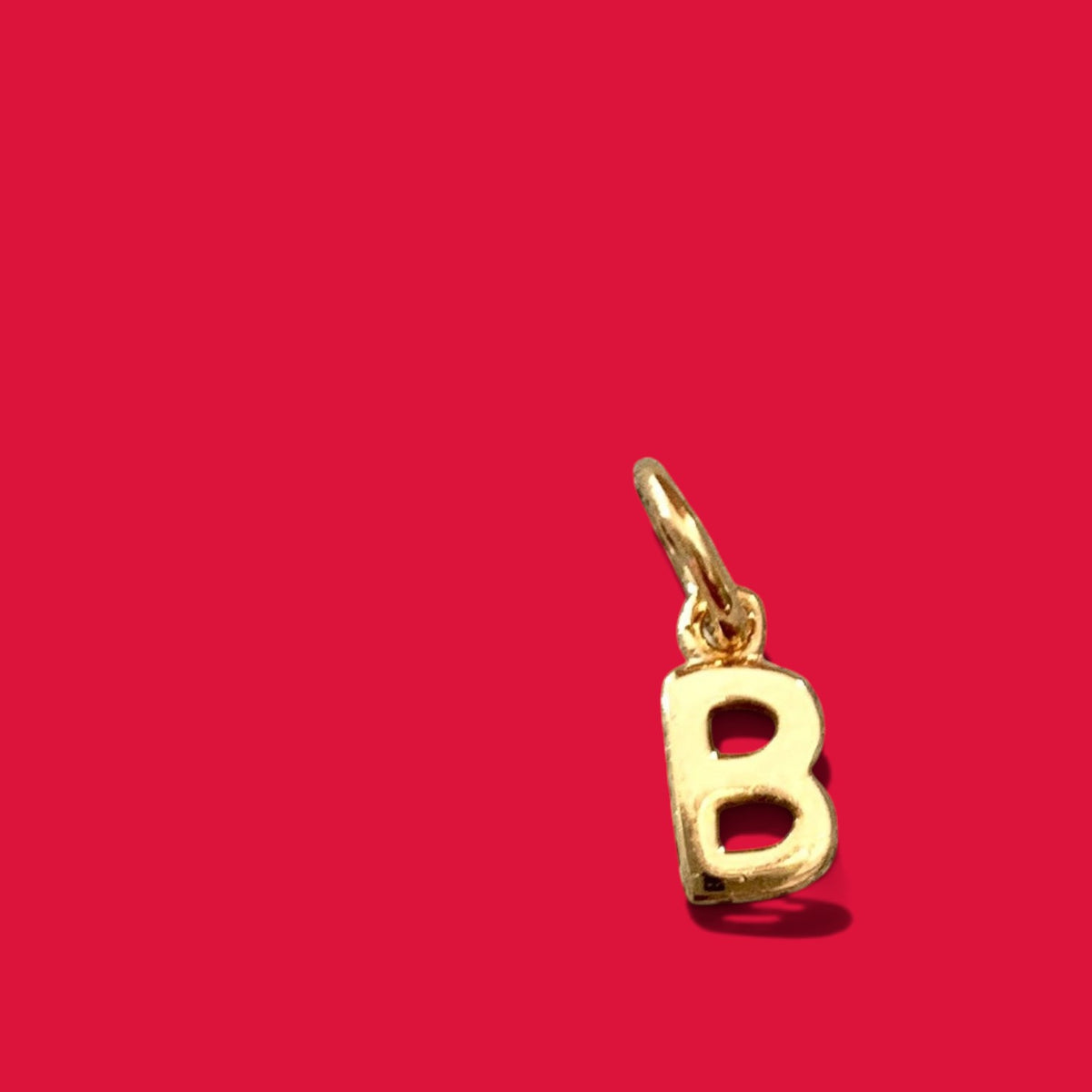 ANNA VON BERGMANN goldplattierter Buchstabenanhänger B aus Messing vor rotem Hintergrund