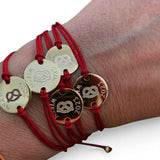 ANNA VON BERGMANN Armband mit roter Nylonkordel und goldplattierter runder Plakette mit Brezel-Gravur am Handgelenk