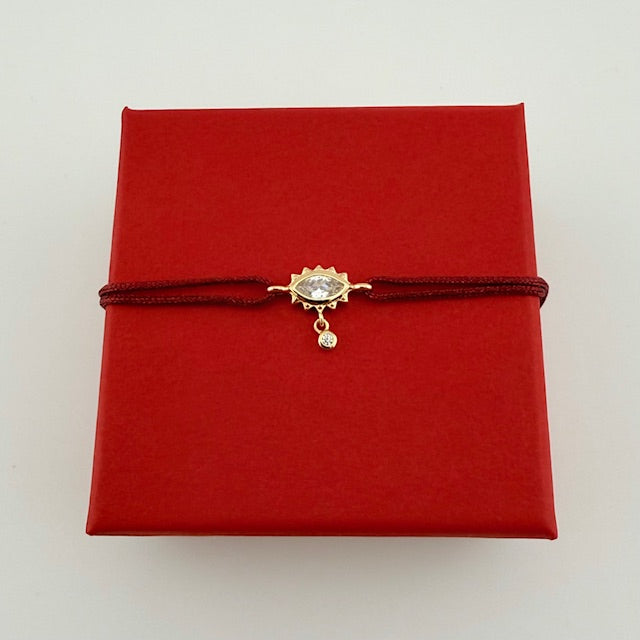 ANNA VON BERGMANN Armband GIDDY aus goldplattiertem Messing, Auge mit Zirkonia an dunkelroter Kordel auf roter Geschenkbox